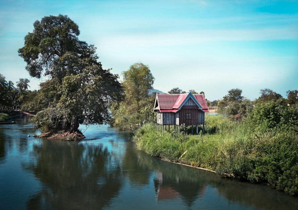 A serene scene of a stilt house on a lush riverbank, reflecting tranquility and nature's beauty.